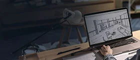 A person using a laptop to design a 3D interior model on a drafting table.        4o