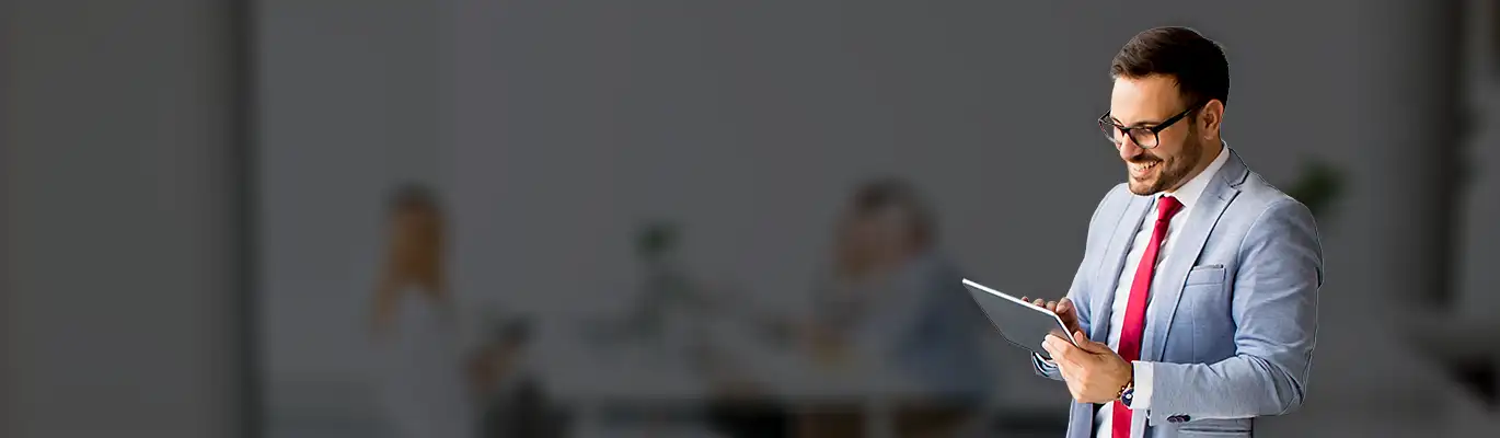 A Project Management Professional Standing with a tablet in hand and looking to it with a smiling face