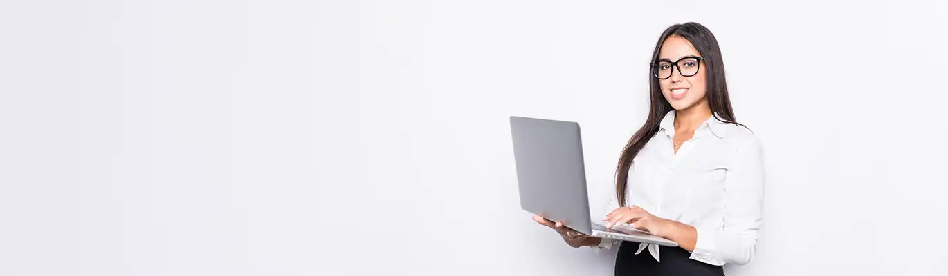 A professional woman in white outfit standing with a laptop in hand in a white background. She is looking into the camera with a smile