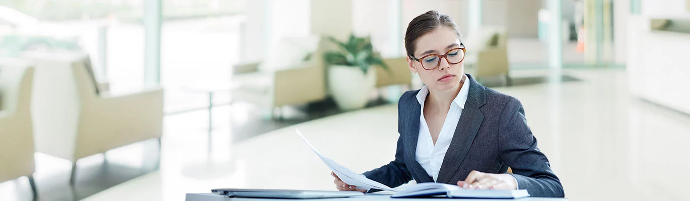 An ERP professional woman sitting with some papers in hand and looking at a book on table