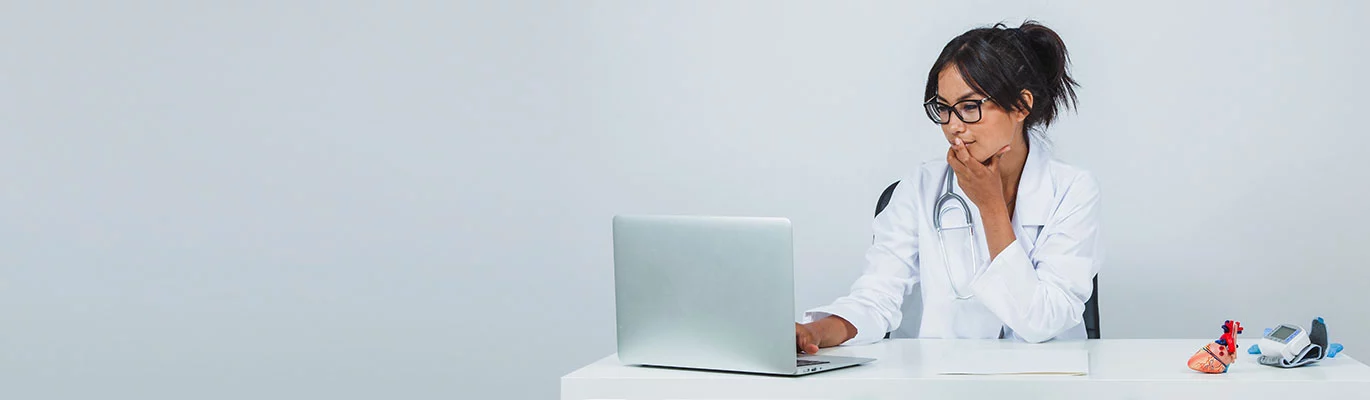 A nursing assistant in uniform sitting infront a laptop 