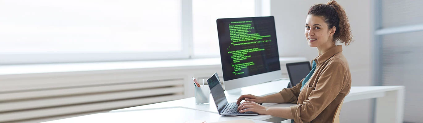 A coding specialist with her laptop and code can be seen running on the screen next to the laptop