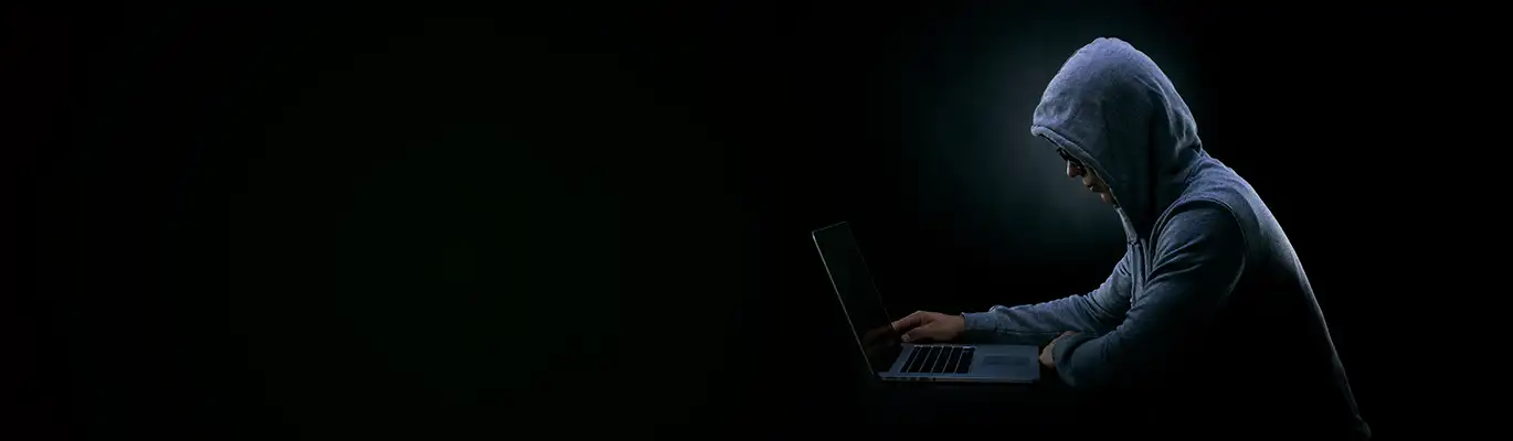 A hacker wearing hoodie sitting in a dark space and working on laptop