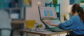 A woman using a dual-screen computer to create digital artwork in a modern office setting.