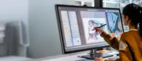 Designer using a stylus to create digital artwork on a large screen in Adobe Illustrator.