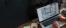 A person working on architectural floor plans using CAD software on a laptop.