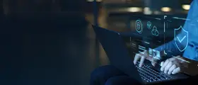 Person using laptop with cybersecurity icons and shield overlay, symbolizing data protection.