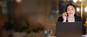 Woman in headset smiling while working on laptop in office.