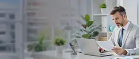 CMA professional in a suit reviewing documents at a desk with a laptop in a modern office setting
