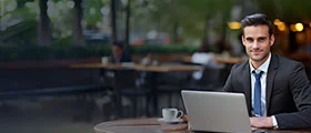 Businessman working on a laptop at an outdoor café, symbolizing remote work or professional training.
