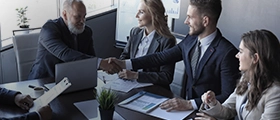 Business professionals in formal attire shaking hands during a meeting in a modern office setting.