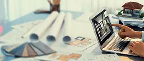 Person working on architectural design on a laptop with blueprints and color samples on a desk.