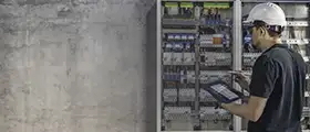 Architect working on a building model with design displayed on a computer screen.