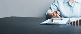 Person calculating finances with a calculator and clipboard, symbolizing accounting or tax preparation tasks.