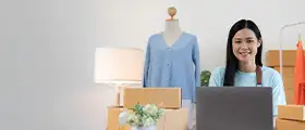 Woman managing an online store with laptop, packaging boxes, and clothing products, representing eCommerce and Amazon FBM business operations.