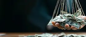 Hand holding U.S. dollar bills suspended by strings, symbolizing money laundering and financial crime.