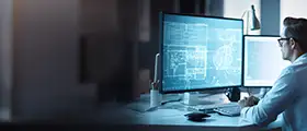 Professional working on AutoCAD Electrical software at a dual-monitor workstation in a modern office environment.