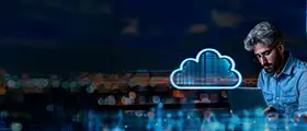 Man working on a laptop with a glowing cloud computing icon, representing cloud technology and data storage over a cityscape at night.