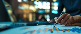 A professional analyzing colorful performance charts on a desk while working on a laptop, representing balanced scorecard strategy and business performance management.