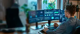 A professional CompTIA Project+ specialist analyzing project dashboards and performance metrics on multiple computer screens in a modern workspace.