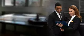 Professional IT specialists in formal attire reviewing information on a clipboard in a server room environment