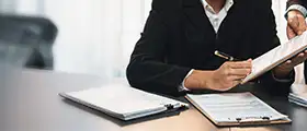 Professional contract management training scene showing business professionals reviewing and signing documents on a table with clipboards and paperwork, symbolizing legal compliance and business negotiation skills.