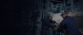 Engineers in protective gear working on industrial equipment in a hydrocarbon production facility