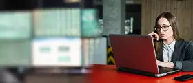 A professional woman in formal attire working on a laptop, representing MS Word course certification training in a modern office environment.