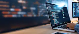 Professional ReactJS developer coding on a laptop with multiple monitors in a modern workspace, representing ReactJS certification training.