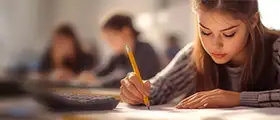 A focused student writing notes with a pencil during exam preparation, with classmates studying in the background, representing SAT course training and test readiness.